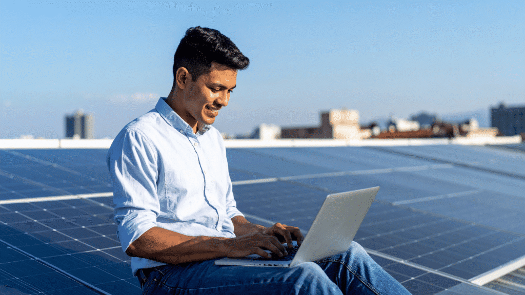 A serene village setting featuring a solar panel installation in the foreground. Close-up view of a technician in modest casual clothing carefully inspecting and maintaining a solar panel, using a multimeter to check the voltage. In the middle ground, several solar panels are arrayed on rooftops, reflecting the sunlight, with lush green trees surrounding the structures. The background showcases a clear blue sky with a few fluffy clouds, creating a peaceful atmosphere. The lighting is bright and natural, capturing the essence of a sunny day. The overall mood conveys diligence and maintenance, emphasizing the importance of safety and care in solar energy usage. ইনস্টলেশনের পর নিরাপদ ব্যবহার, রক্ষণাবেক্ষণ ও সাধারণ সমস্যা সমাধান